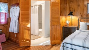 A wooden room with a bed, a nightstand, a bedside lamp, a wooden wardrobe, and a bathroom visible through an open door. - Inn at Sugar Pine Ranch (Groveland)
