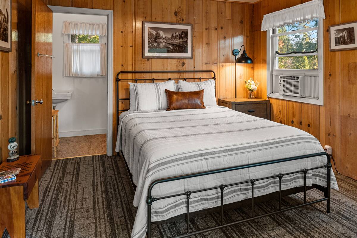 Un dormitorio con paneles de madera, una cama, una mesita de noche, una lámpara y una ventana con cortinas.