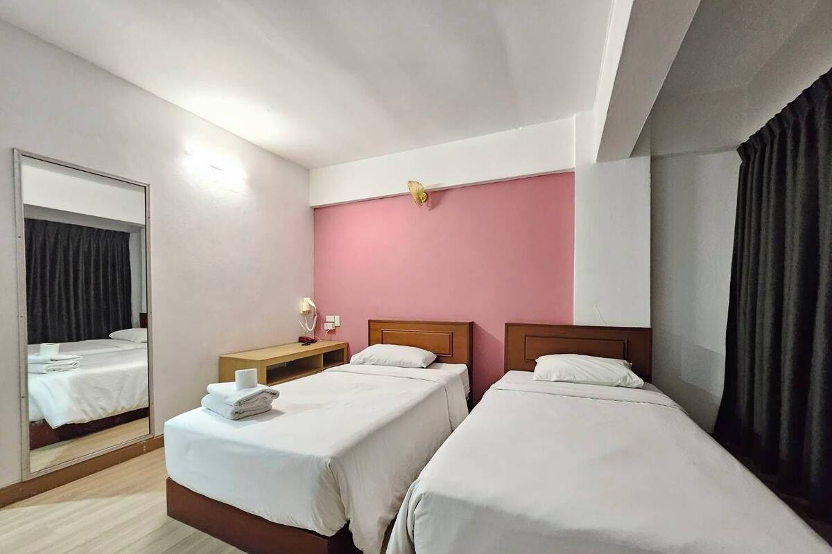 Ein Hotelzimmer mit zwei Betten, einem Spiegel, einem Nachttisch mit Lampe und einer Wand in Rosa.
