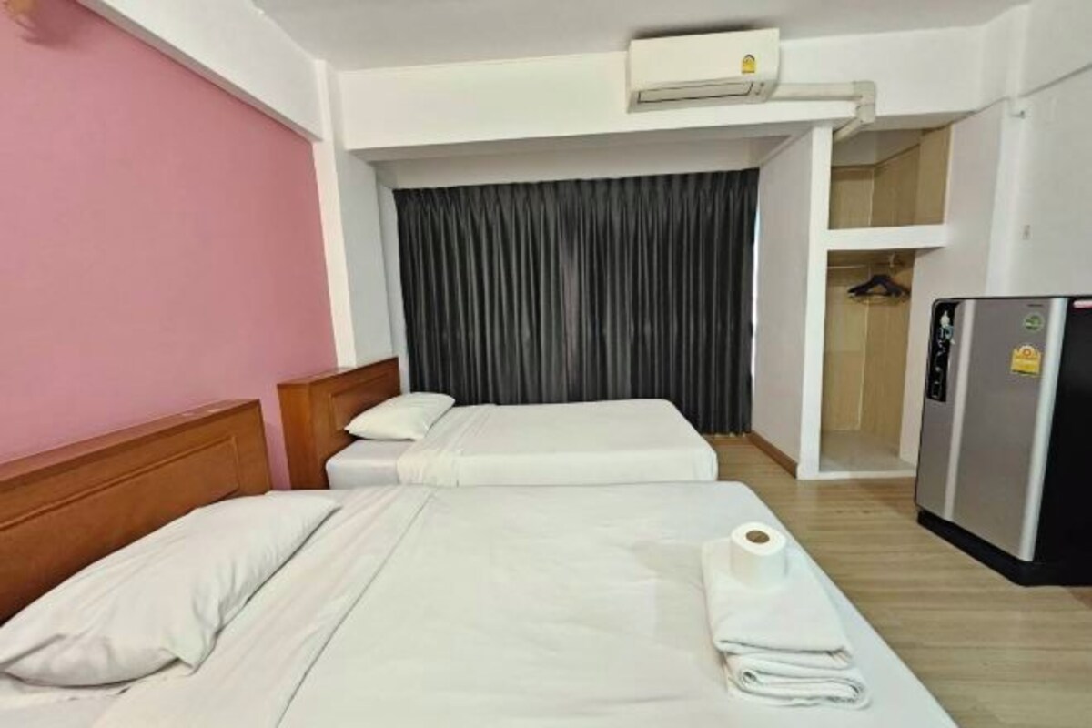 A hotel room with two beds, a refrigerator, an air conditioning unit, and a curtain.