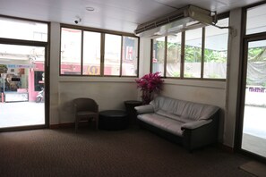 A room with a sofa, a chair, and a small table. There is a window with a view of the outside. - Crown   Bts   Nana  Hotel (Bangkok)