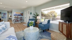 A modern living room with a large window, a television, and a bicycle in the background. - Beach View Bungalow with Stunning, Panoramic Views (Encinitas)