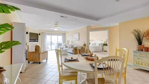 A spacious living area with a dining table set for four, a sofa, and a TV in the background.