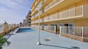 A multi-story hotel with balconies, a swimming pool, and a paved walkway.