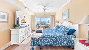 A bedroom with a bed, a dresser, a ceiling fan, and a window with a balcony view.