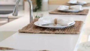A kitchen with white cabinets, a stainless steel sink, and a long countertop with placemats and plates.