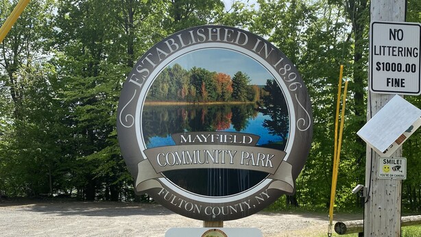 A sign for Mayfield Community Park with a scenic lake view, a no littering sign, and a notice about government property.