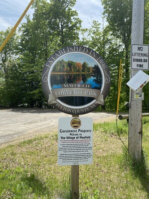 A community park sign with a scenic lake view, a no littering sign, and a welcome sign for Mayfield Community Park in Fulton County, NY. - Experience the Adirondacks (Mayfield)