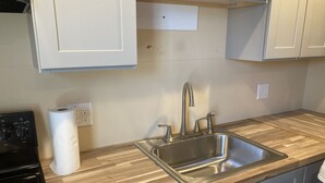 A kitchen with a stainless steel sink, wooden countertop, and white cabinets.