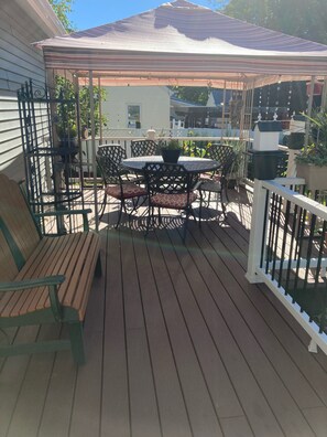 A wooden deck with a round table and chairs, surrounded by potted plants and a white railing. - Experience the Adirondacks (Mayfield)