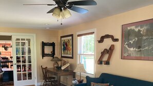 A living room with a blue sofa, a patterned rug, a ceiling fan, and a dining area with a table and chairs.
