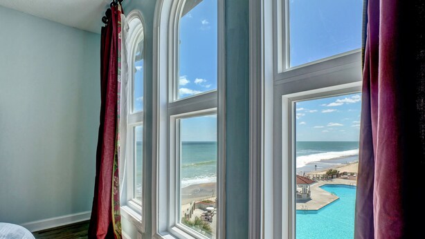 Een kamer met een groot raam met uitzicht op een strand en een zwembad.