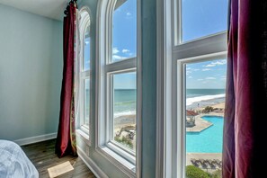 Una habitación con un amplio ventanal que da a una playa y una piscina.