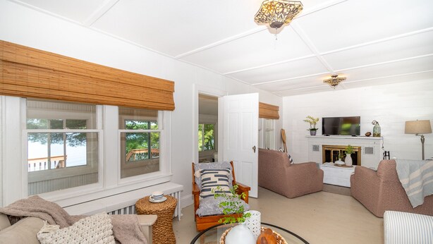 A cozy living room with a fireplace, comfortable seating, and large windows overlooking a deck. - The Congamond Cottages: Private Lakefront Cottage (Suffield)