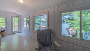 A room with large windows, a wooden floor, and a chair with a patterned cover. - The Congamond Cottages: Private Lakefront Cottage (Suffield)