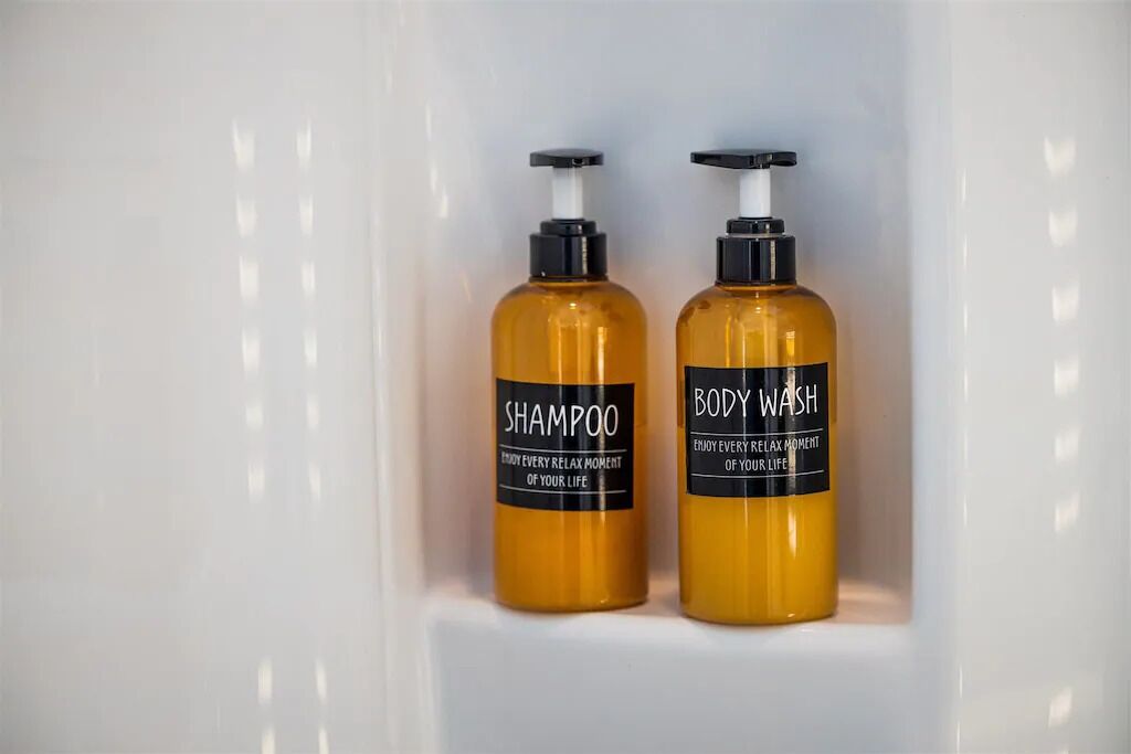 Twee flessen douchegel en shampoo op een wit schap.