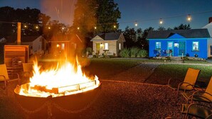 A fire pit with chairs around it, a blue house, and string lights in the background. - Whimsical Tiny House, Cape Charles Virginia (Cape Charles)