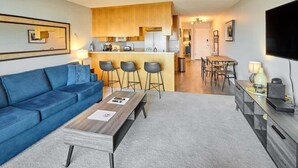 A modern living room with a blue sofa, a wooden coffee table, and a kitchen area with bar stools. - Updated Oceanfront Condo -Ground Floor- Fireplace! (Lincoln City)
