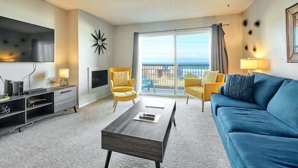 A modern living room with a sofa, armchairs, a coffee table, a TV, and a balcony with a view. - Updated Oceanfront Condo -Ground Floor- Fireplace! (Lincoln City)