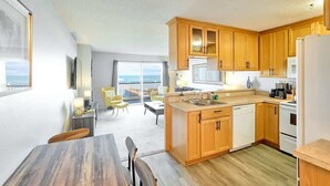 A modern kitchen with wooden cabinets, a dishwasher, and a refrigerator. There is a dining area with a table and chairs. - Updated Oceanfront Condo -Ground Floor- Fireplace! (Lincoln City)