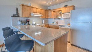 A modern kitchen with wooden cabinets, a large island, a refrigerator, and a microwave. - Ocean View Condo - Second Floor - Pet Friendly! (Lincoln City)