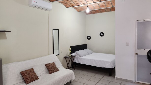 A small, clean room with a white sofa, a single bed, a wall-mounted air conditioner, and a ceiling fan. - Coral House II (Sayulita)