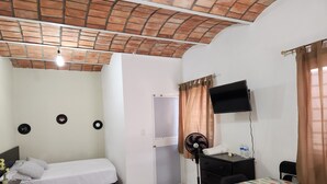 A room with a bed, a desk, a chair, a TV, a fan, and a door. - Coral House II (Sayulita)
