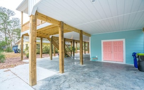 A covered porch with wooden beams, a concrete floor, and a pink door.