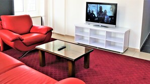 A living room with a red leather sofa, a glass coffee table, and a white entertainment unit with a flat-screen TV.