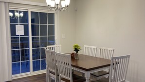A dining room with a wooden table and white chairs, a chandelier, and a sliding glass door leading outside. - Furnished 1 bedroom (Front Royal)