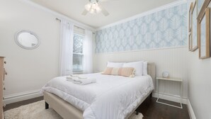 Een slaapkamer met een bed, nachtkastje, spiegel en een raam met gordijnen.
