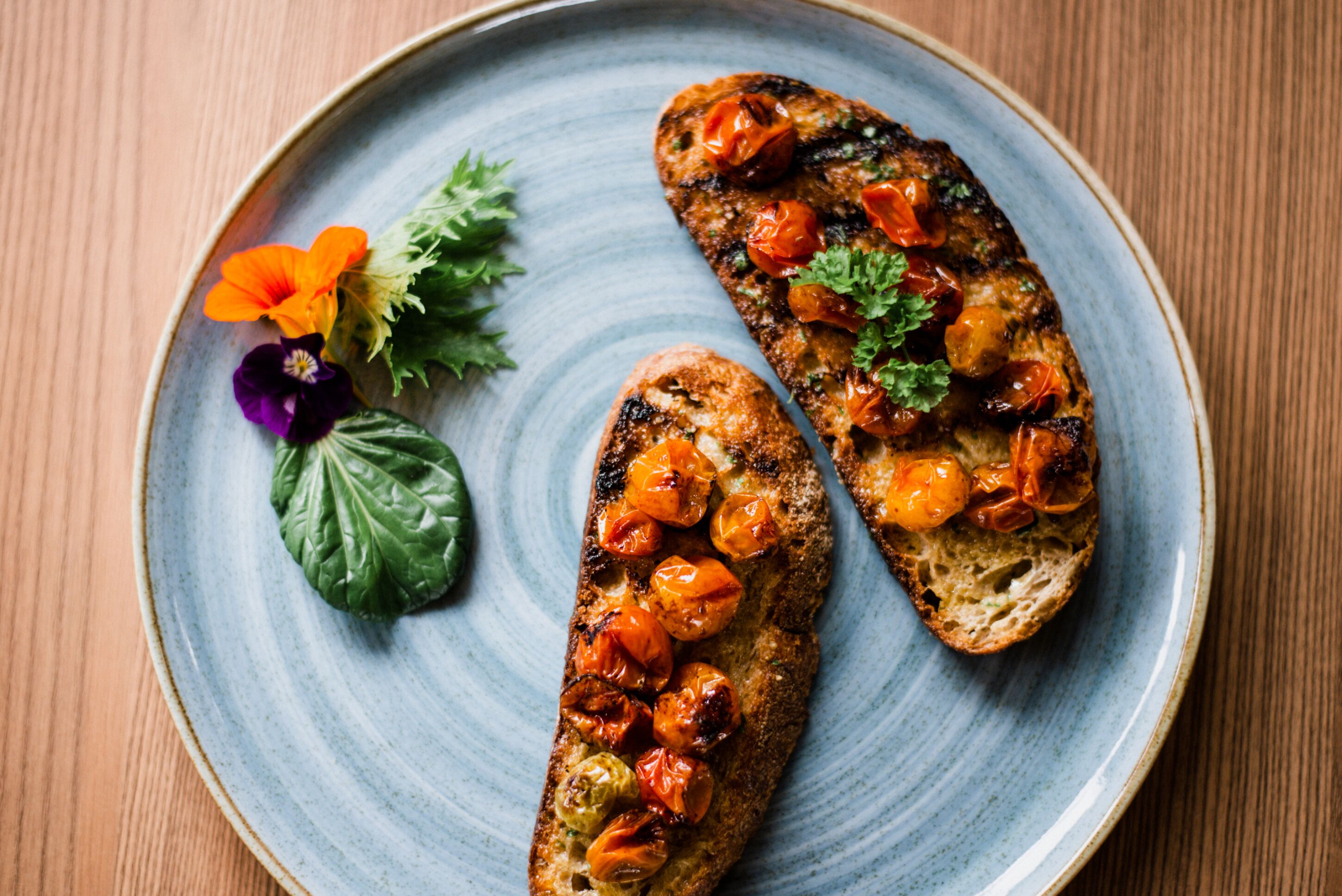 Two pieces of grilled bread with tomatoes and herbs on a ceramic plate.