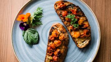 Two pieces of grilled bread with tomatoes and herbs on a ceramic plate.