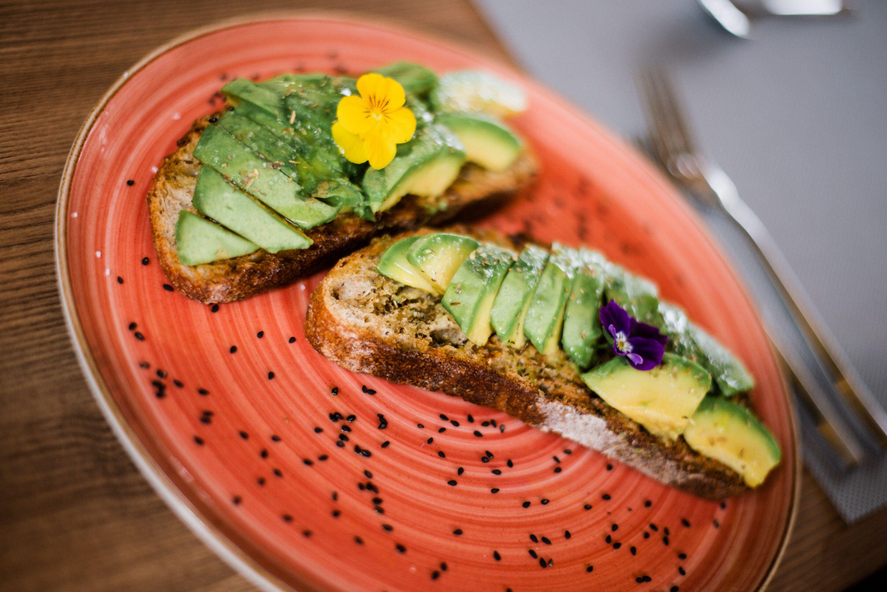 Two slices of toast with avocado and sesame seeds on a red plate.