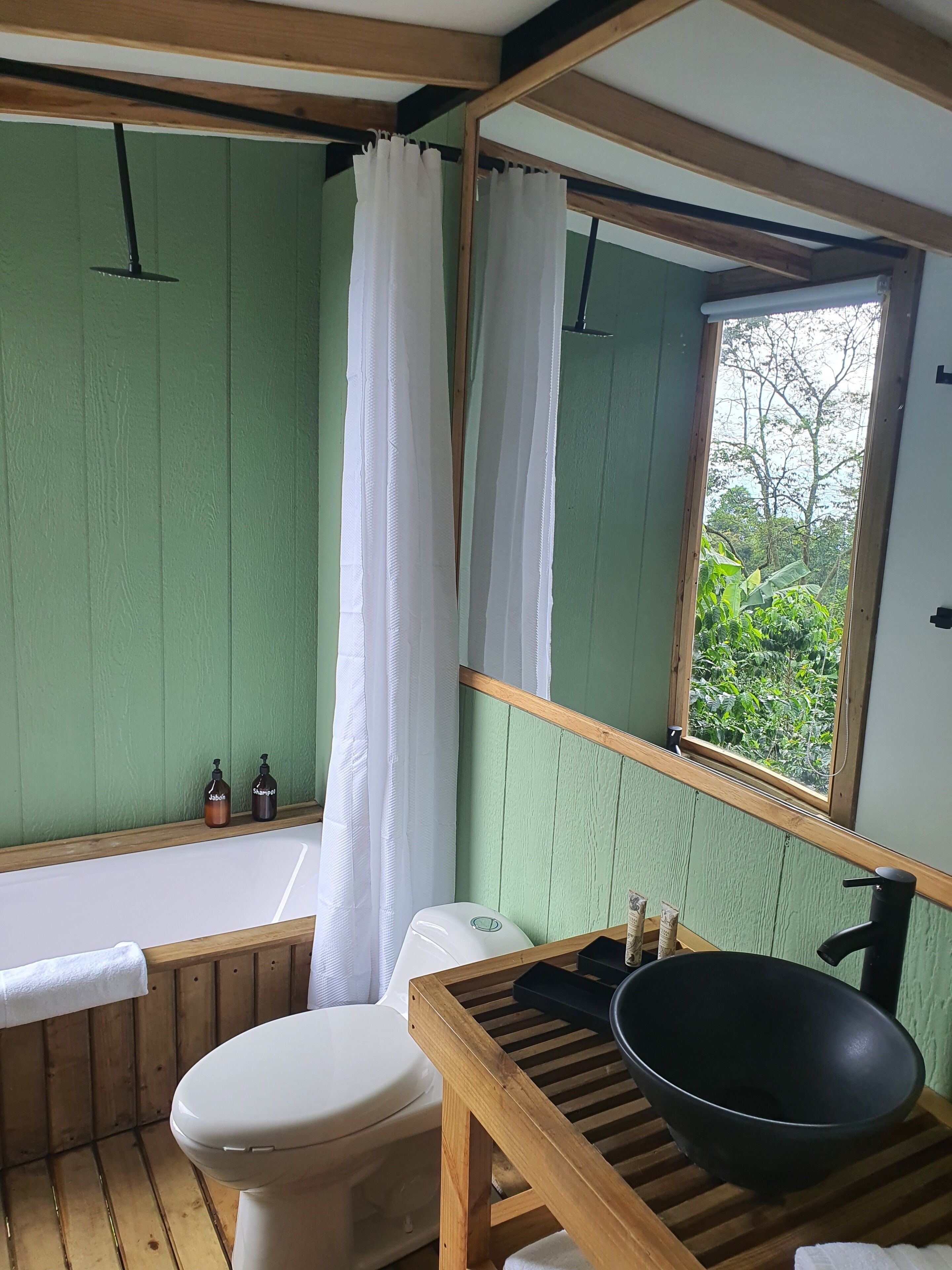 Casa de banho com toucador em madeira, sanita branca, banheira e janela com vista para vegetação.