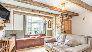 A cozy living room with exposed wooden beams, a leather sofa, a wooden table, and a window with a view. - 48 High Street (Bridlington)