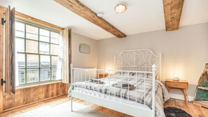 A bedroom with a white metal bed frame, a large window with wooden shutters, a wooden floor, and a small bedside table with a lamp. - 48 High Street (Bridlington)