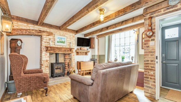 A cozy living room with a fireplace, wooden beams, a sofa, a chair, and a television. - 48 High Street (Bridlington)