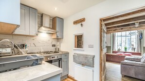 A kitchen with grey cabinets, a built-in oven, and a window overlooking a living area with a sofa. - 48 High Street (Bridlington)