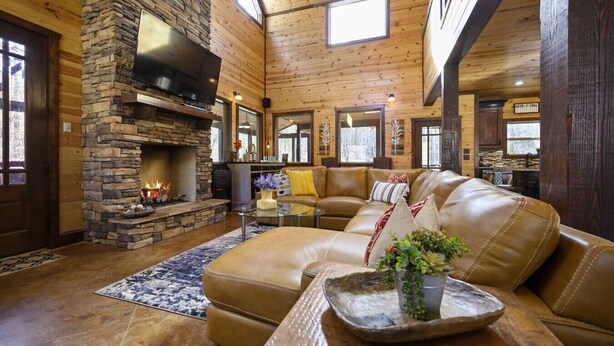 Un interior de cabaña acogedor con chimenea de piedra, sofá de cuero y comedor.