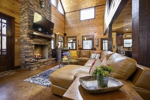 A cozy cabin interior with a stone fireplace, leather sofa, and a dining area.