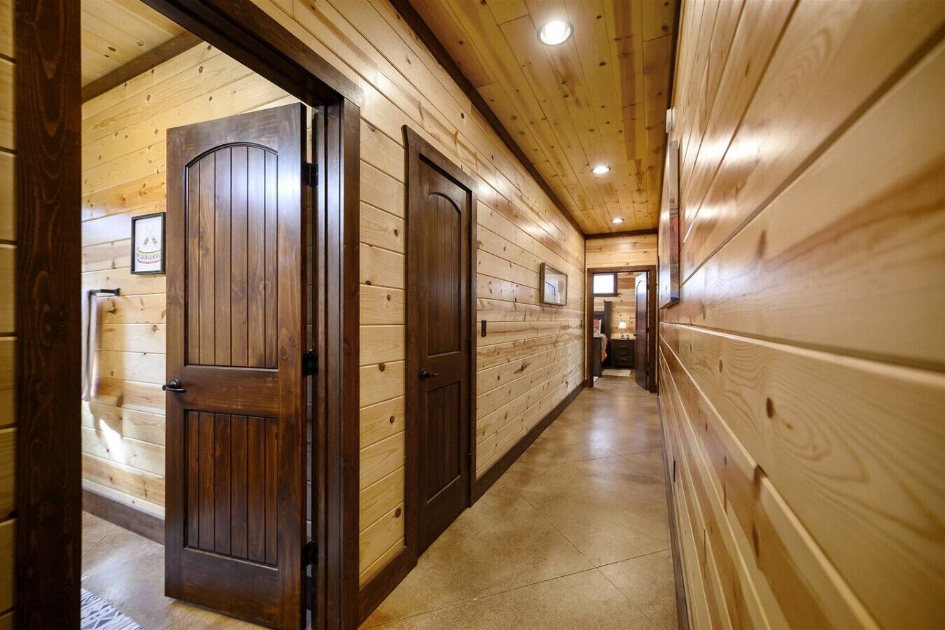 A wooden hallway with two doors, a tiled floor, and a ceiling with recessed lighting.