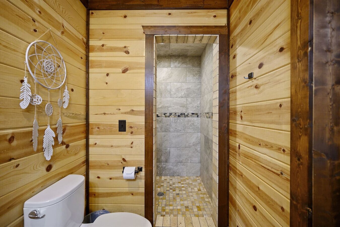 A wooden cabin bathroom with a toilet, dreamcatcher, and a shower area.