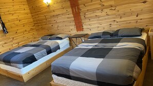 A wooden cabin room with two beds, a small table, and a wall-mounted light fixture. - Cabin in Little Cove Adventure park, Tobermory  Cabin 14 (Tobermory)