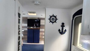 A narrow hallway with a kitchen area at the end, featuring a blue cabinet, a ship's wheel, and an anchor decoration on the wall.
