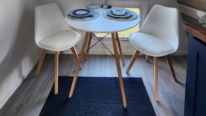 A compact RV interior with a dining area featuring a round table, two chairs, and a small window.
