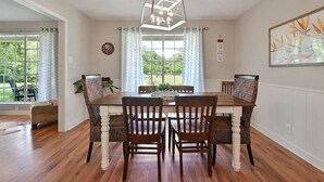 Comedor con mesa y sillas de madera, una lámpara de araña y vistas al exterior.