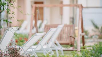 Un jardín con sillones de sol, una mecedora de madera y diversas plantas.