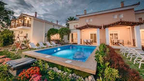Area piscina con lettini, un pontile in legno e un edificio con un balcone.