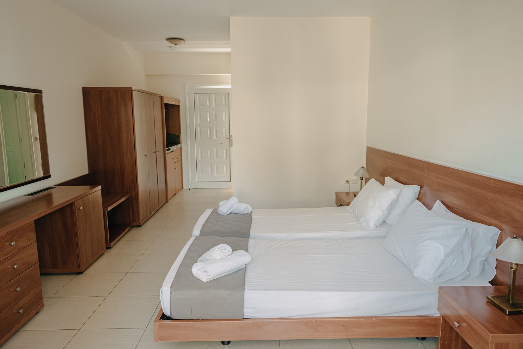 A hotel room with a large bed, wooden wardrobe, a desk, and a television.